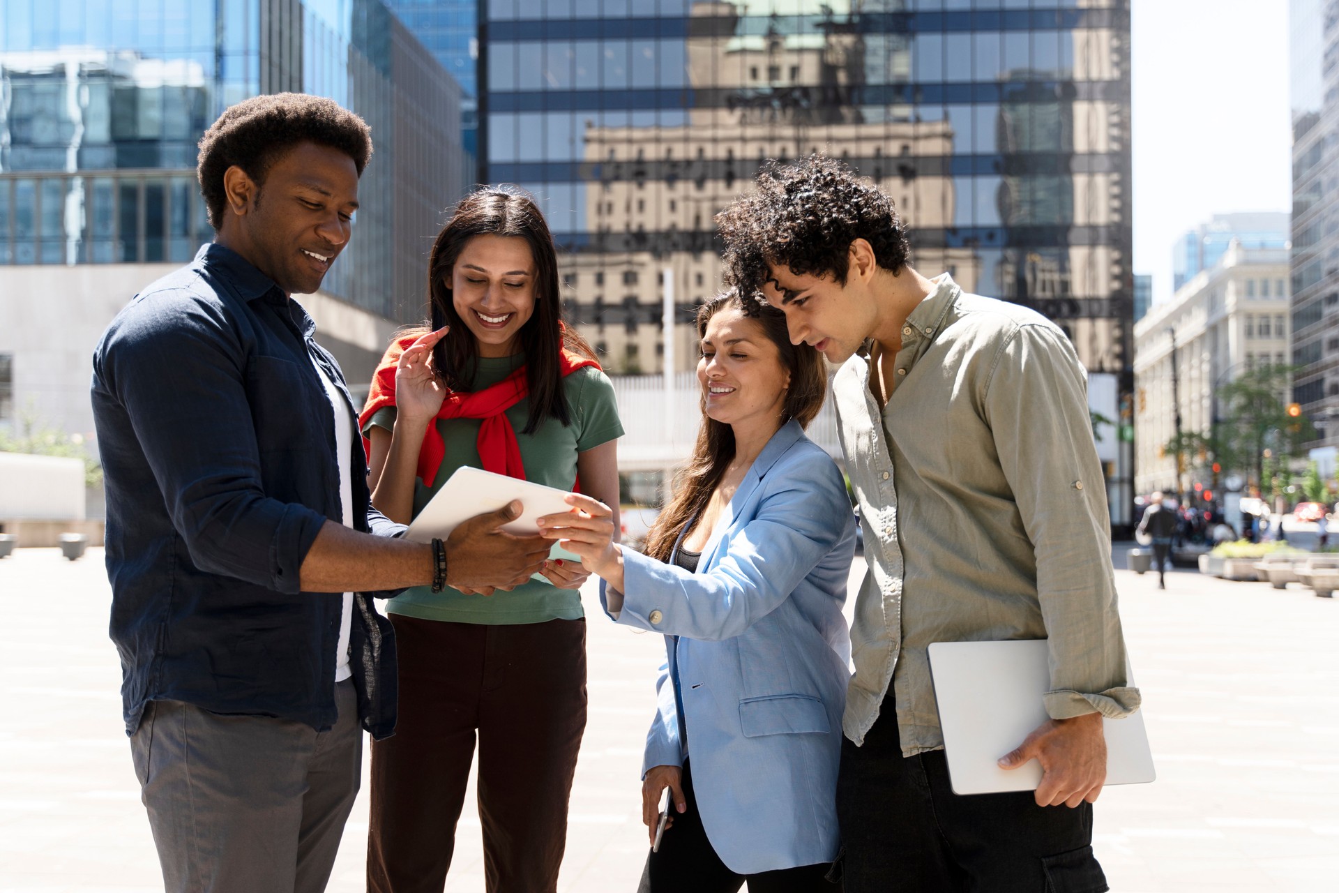 Group of diverse businesspeople collaborating around tablet outdoors in the city
